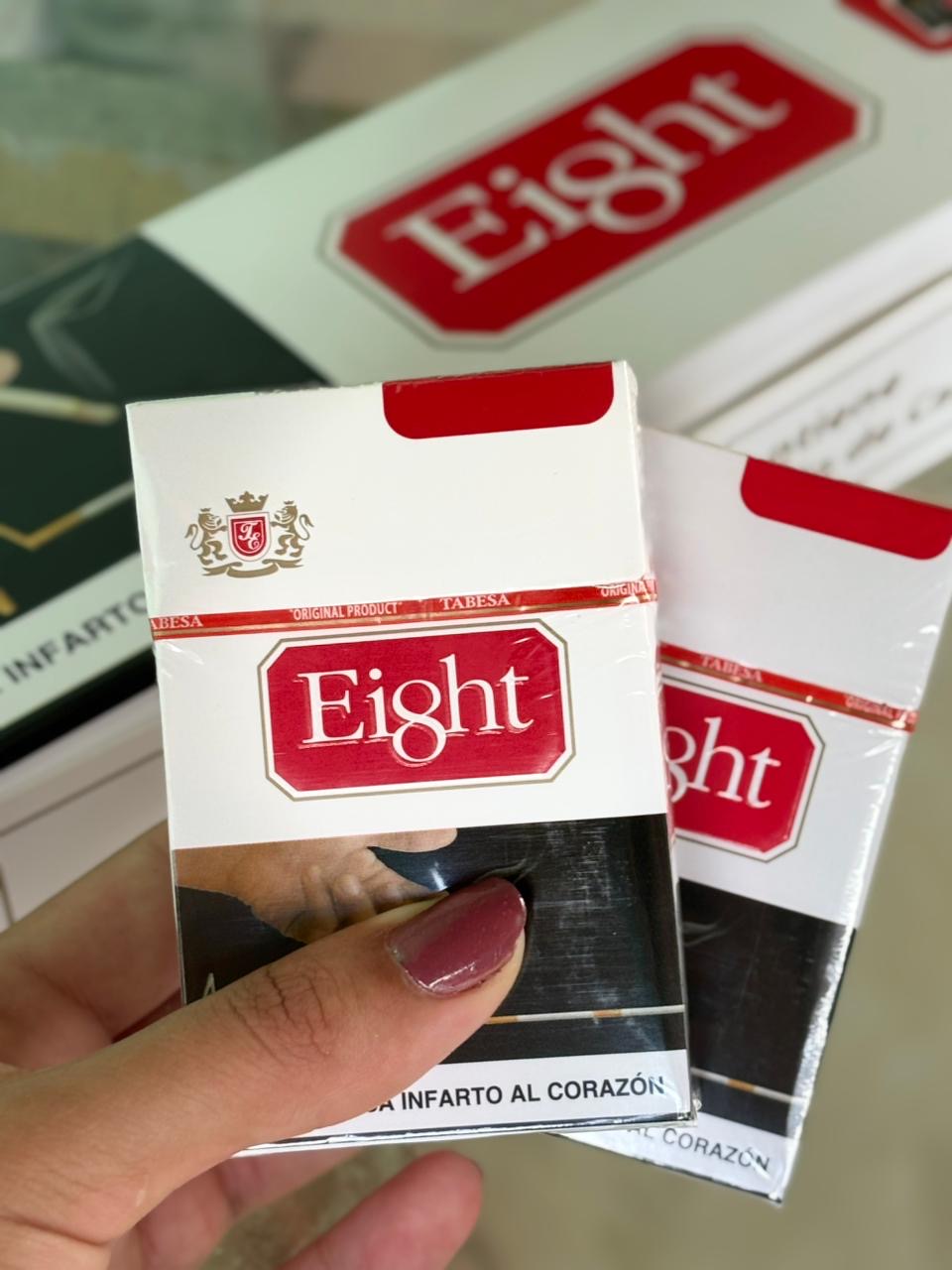 Pacote de cigarro oito branco e vermelho com logo em ouro e imagem preto e branco na parte inferior