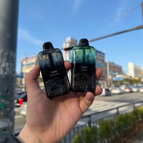 Dois vape pens duke elfbar 35k em degradê preto e azul mineral water e verde-azulado korean mint na mão