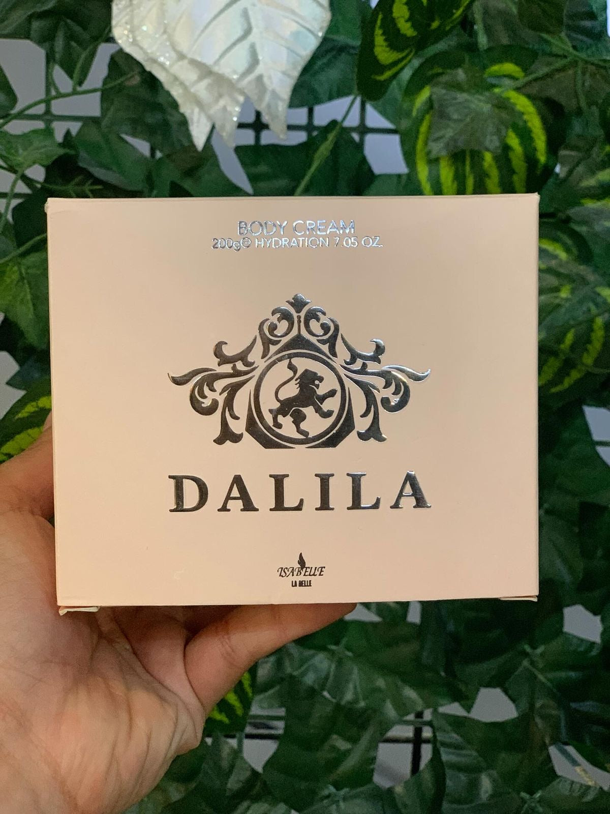 Caixa retangular bege do creme corporal dalila isabelle la belle com logo de leão prateado e nome da marca em letras escuras