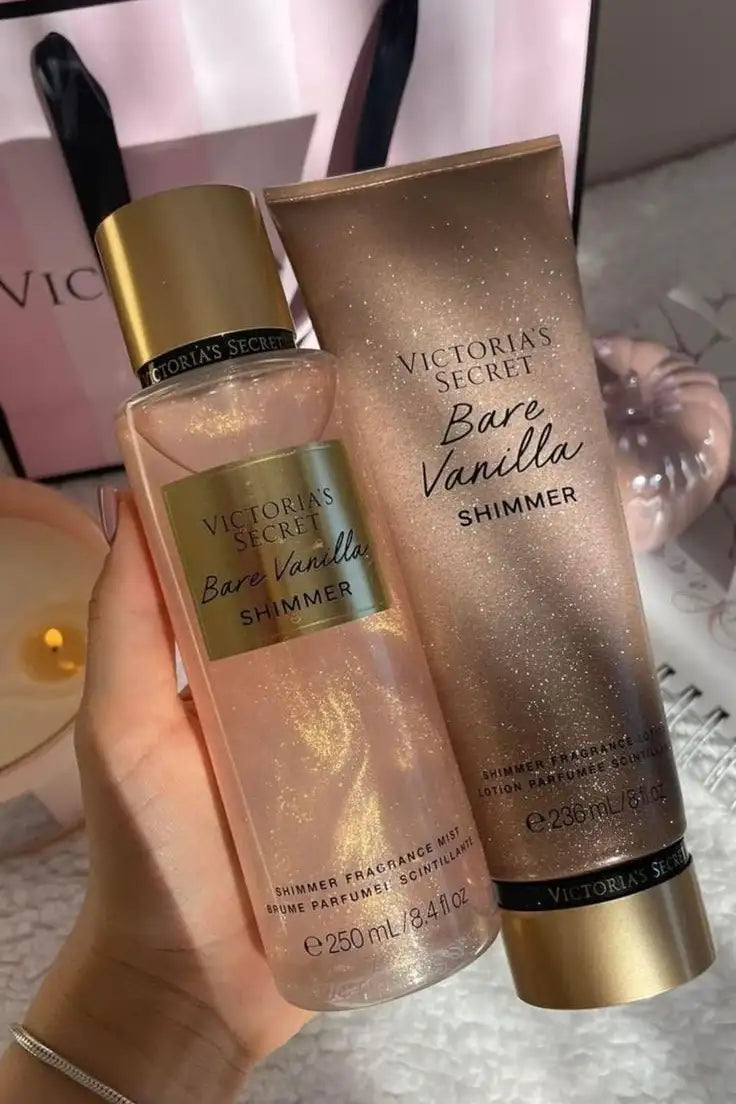 Uma mão segura um frasco transparente de neblina de fragrância bare vanilla shimmer da Victoria's Secret com detalhes dourados e líquido rosa brilhante, com glitter, ao lado da loção corporal shimmer correspondente, em um tubo de tom rosé.