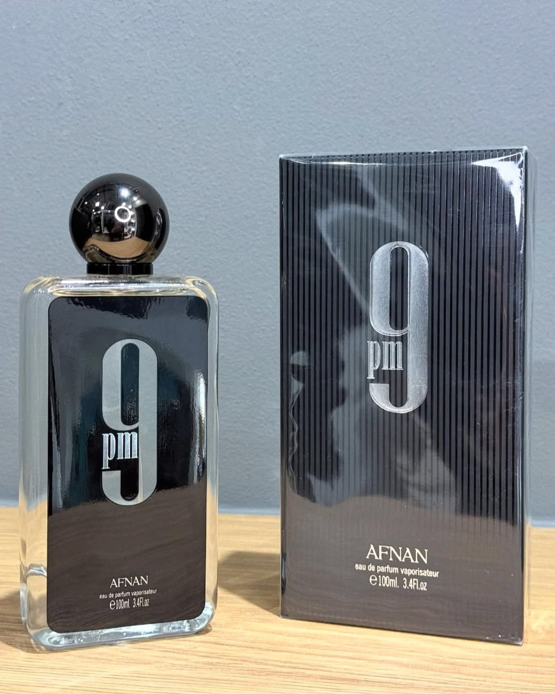 Perfume 9 pm afnan eau de parfum masculino em vidro preto com tampa preta brilhante e logo prata ao lado da caixa correspondente