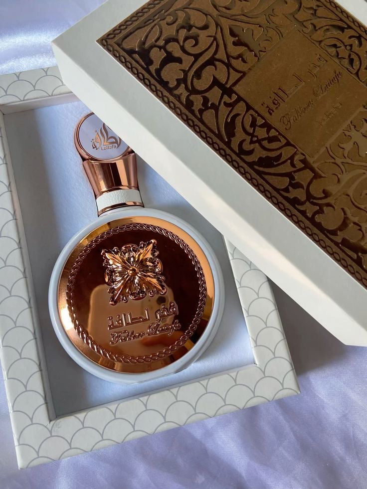 Frasco de perfume lattafa fakhar rose em tom rose gold com design floral em relevo e tampa circular com escrita árabe