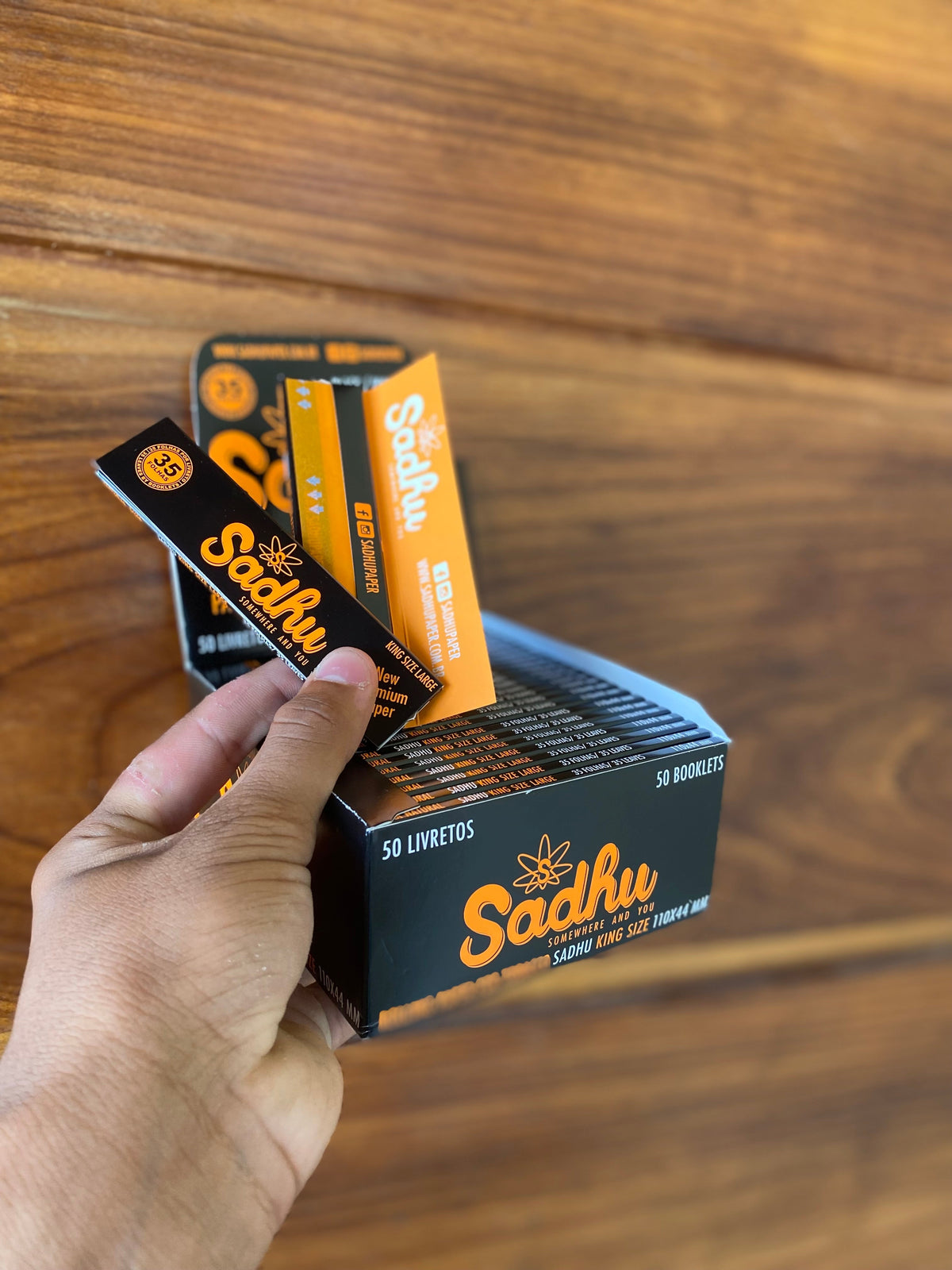 Caixa com 50 maços de seda sadhu large king size nas cores preta e laranja para enrolar cigarros