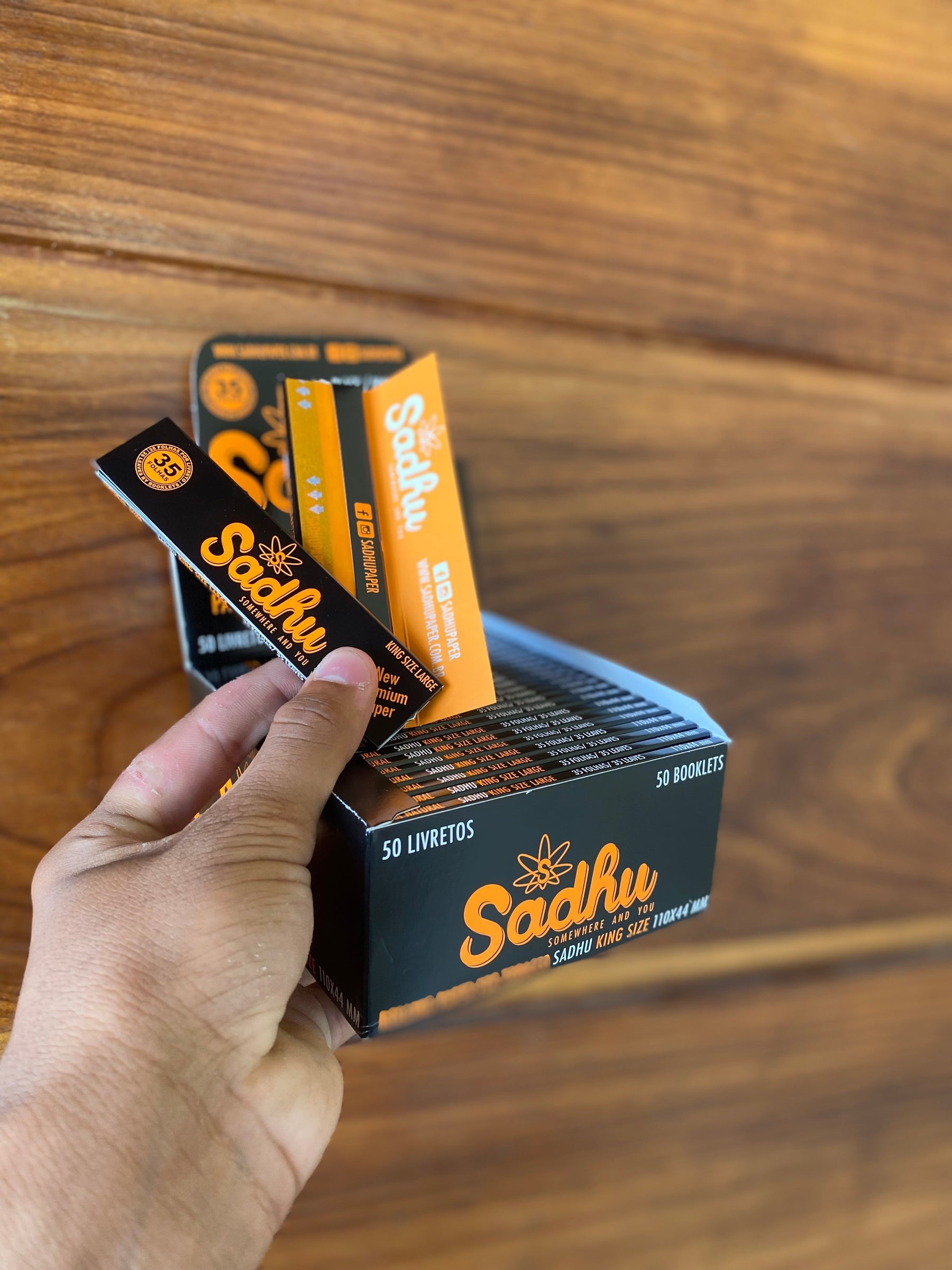 Caixa com 50 maços de seda sadhu large king size nas cores preta e laranja para enrolar cigarros