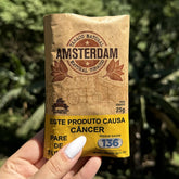 Pacote marrom de tabaco natural amsterdam 25g com design vintage e etiqueta amarela de advertência